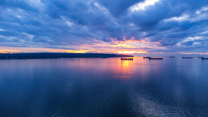 Sunset over Burrard inlet. Sun dipping behind peniunsula. Container ships sit in the calm ocean....