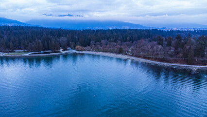 Stanley Park Seawall. Clouds reflect off a calm ocean. North Shore mountains in the background. 