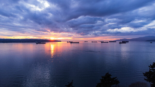 Container ships set against setting sun. Vancouver, BC, Canada
