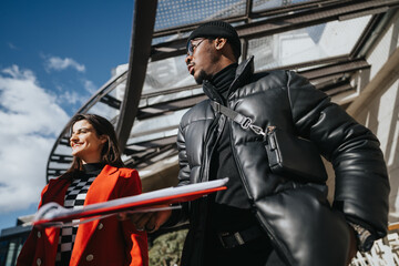Two business people in smart winter attire conversing while holding documents, showcasing teamwork and partnership in an urban setting.