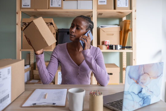 Black manager reading label on box during phone call
