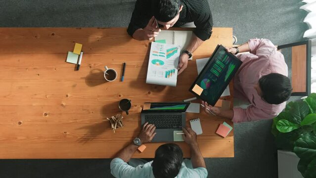 Smart project manager calling phone while diverse team brainstorm idea and looking at financial statistic at tablet at meeting table. Diverse business people planning marketing strategy. Convocation.