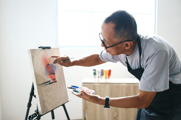 Asian senior man wear glasses, painting picture using brush and oil color on canvas