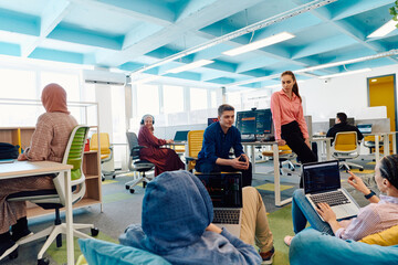 In a modern startup office, a diverse group of young and capable businesspeople engage in lively...