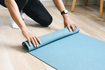 Man standing on knees and rolling exercise mat after yoga training at home - obrazy, fototapety, plakaty