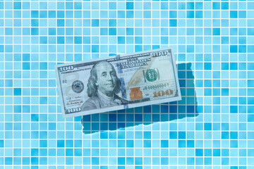 100 dollar bill floating in clear swimming pool water.