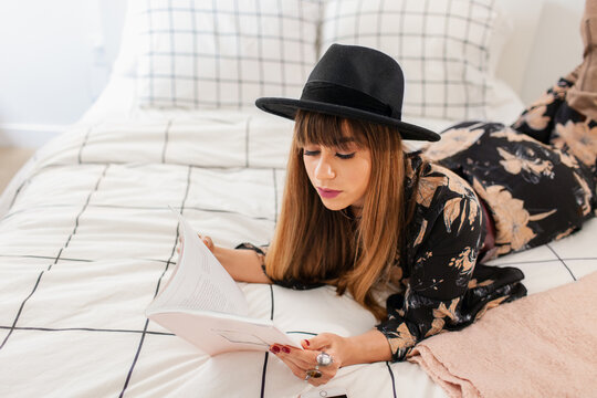 Studious hipster woman reading from the bed