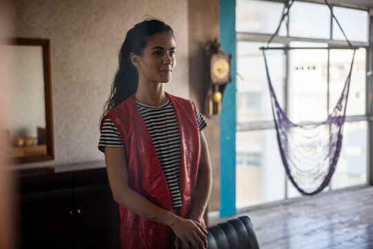 Dimly lit portrait of young woman near hammock and old watch indoors