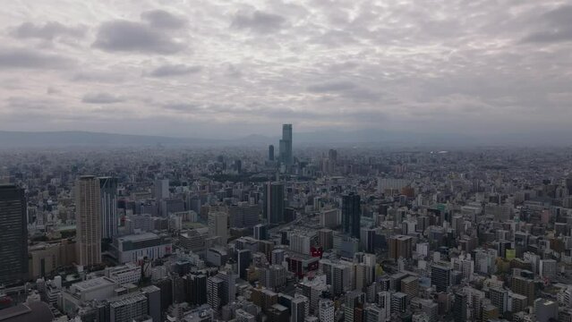 Forwards fly above large city. Aerial panoramic footage of metropolis under cloudy sky. High density of town development. Osaka, Japan