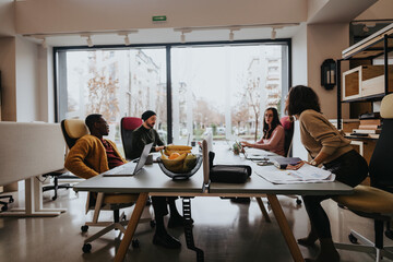 Mixed race team of males and females businesspeople engaged in discussion at modern office space with large windows.
