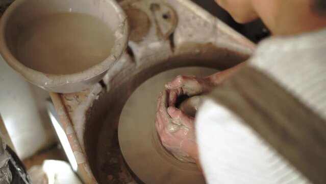 Slow motion, overhead view of a female potter beginning to open clay to form a vessel on a spinning wheel.