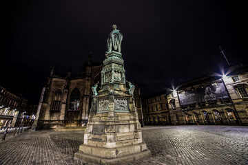 A statue in a middle of a square illuminated at night. - Powered by Adobe