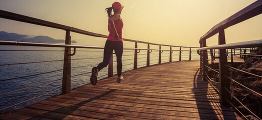 Healthy lifestyle sports woman running on wooden boardwalk seaside