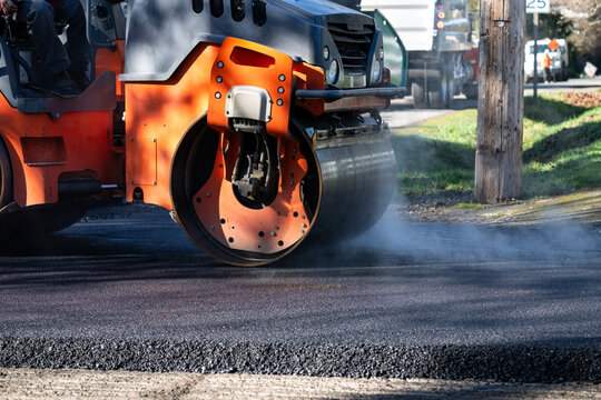 Closeup of steam roller compacting freshly paved asphalt with smoke and steam © knelson20