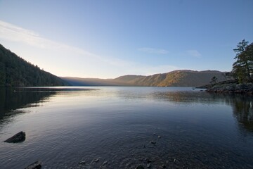 Fototapeta premium The tranquil waters of a calm lake mirror the fading hues of the day, set against a backdrop of majestic mountains in the distance.