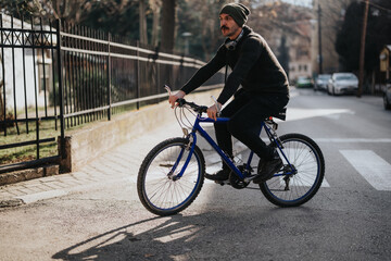 Fototapeta premium A stylish young man with headphones cycling on a vibrant blue mountain bike in an urban setting with sunlight illuminating the scene.