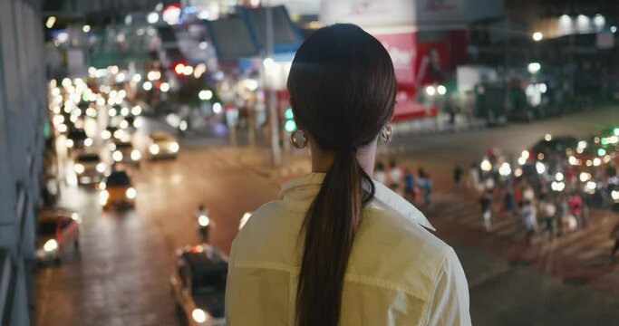 Woman looking at bustling traffic at night in big metropolis back view close-up Traffic pulse of city. Traffic stream of never-ending activity Illustrating non-stop nature of urban life.