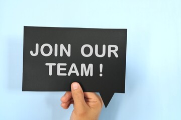 Human hand holding black speech bubble with written phrase Join Our Team. Recruitment and job hiring concept.
