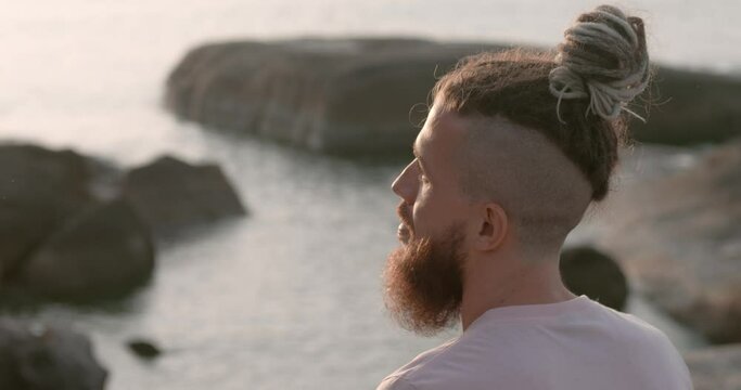 Man with beard sitting calmly on beach at sunset side view close-up. Thoughtfulness in tropical serenity Thoughtfulness sign of summer's calm Thoughtfulness reflecting on life's beauty.
