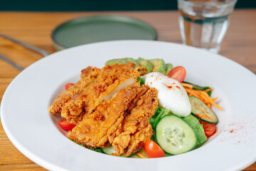 A plate of fried chicken salad with a glass of water