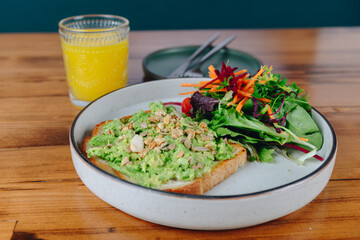 A plate of food with a sandwich and a salad sits on a wooden table