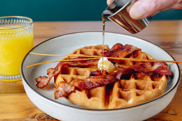 A plate of bacon and waffles with syrup poured on top