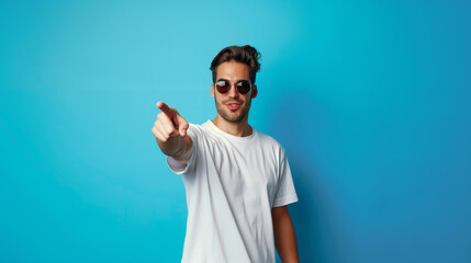 Naklejka premium 20s white man with sunglasses and white t-shirt pointing with his finger on blue background 