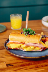 A sandwich with ham and cheese on a blue plate with a glass of orange juice