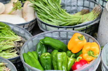 The traditional market stall offers a variety of fresh vegetables - a basket of colorful bell peppers: green, red, and yellow.