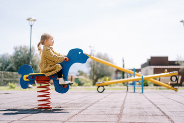 Little girl swings on a spring swing on the playground. Side view