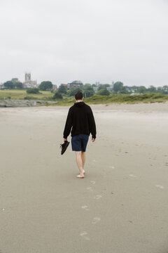 millennial man walking barefoot on beach in rhode island