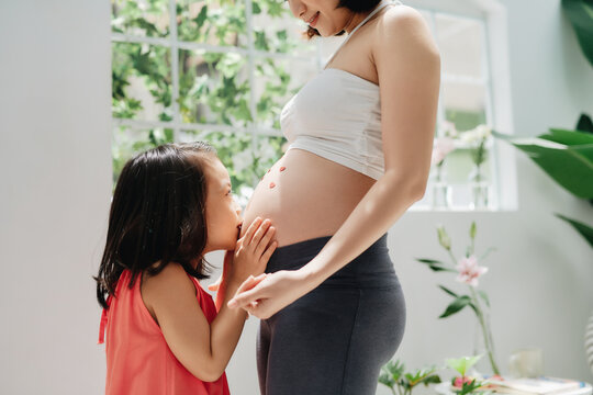 Young pregnant woman and her little daughter kissing her belly