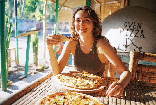 Cheerful woman eating pizza and looking at camera