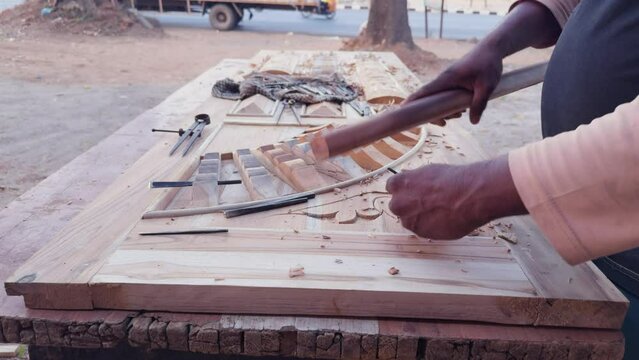 Artisan hands carving wood with chisel on workbench with tools and wood shavings around