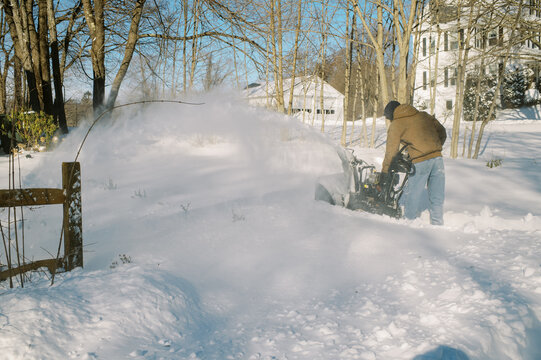 millennial man snow blowing his property after snow storm