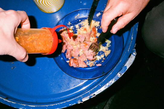 Man eating street food at night adding spicy sauce to his bbq dish