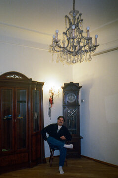 Man sitting in front of antique furniture: longcase clock and cupboard