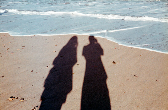 The Silhouettes Of A Couple Projected Onto The Sand Near The Seashore
