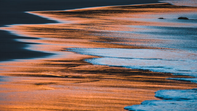 waves creating beautiful abstract patterns in the sand at sunset