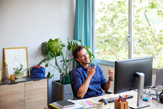 Male freelancer recording audio message at desk with PC