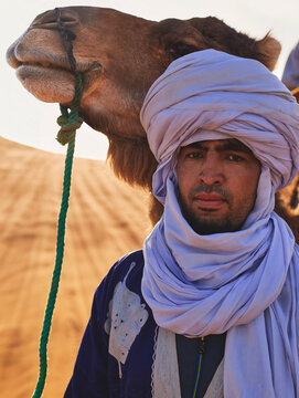 young tour guide wearing a turban, with a camel in the Sahara desert.