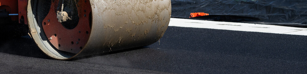 Closeup of steam roller compacting freshly paved asphalt with dirty water lubricating the roller
