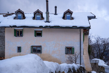 Part view of a snow-covered traditional Engadine house,  with dormer windows in Bos-Cha,...