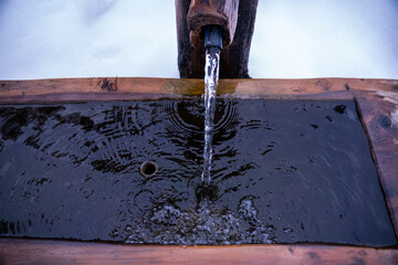 Close-up of a stream of water from a natural spring into the wooden trough of a cattle trough. ...
