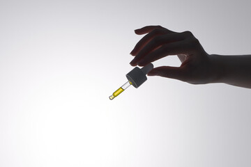 Hand of woman with pipette drop of serum or hyaluronic acid on gray ba