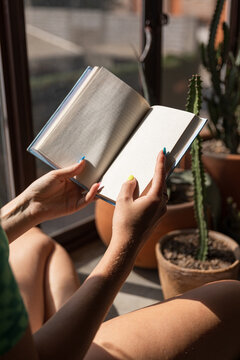 An anonymous woman reading a book next to a window