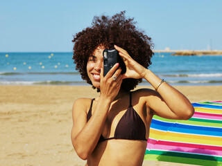 Say cheese: smiling woman with afro and bikini taking photo at beach