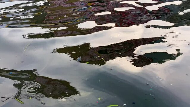 Rippling water reflecting abstract urban images, vibrant colors, with floating debris