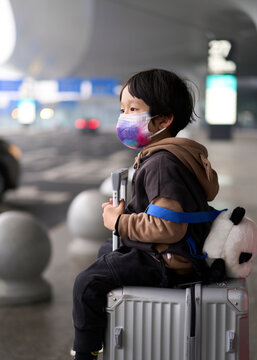 Asian little boy sitting on suitcase waiting for taxi, at airport