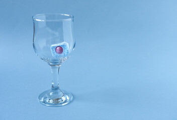 Wine glass with dishwasher tablet. Wine glass with dishwasher tablet on light blue background. 